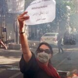 زنی در خیایان در میانه اعتراضات نوشته ای در دست دارد با شعار زن زندگی و آزادی