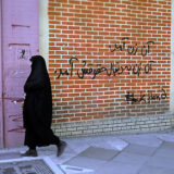 تصویری از یک گرافیتی (دیوارنگاری) با عنوان «آن زن آمد، آن زن به‌دنبال حقوقش آمد». یک زن با حجاب چادر از جلوی این دیوار در حال گذشتن است.
